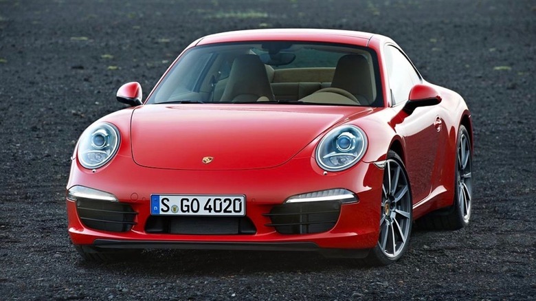 A red Porsche 911 from the 991.1 generation released in 2011 standing on gravel in the evening.