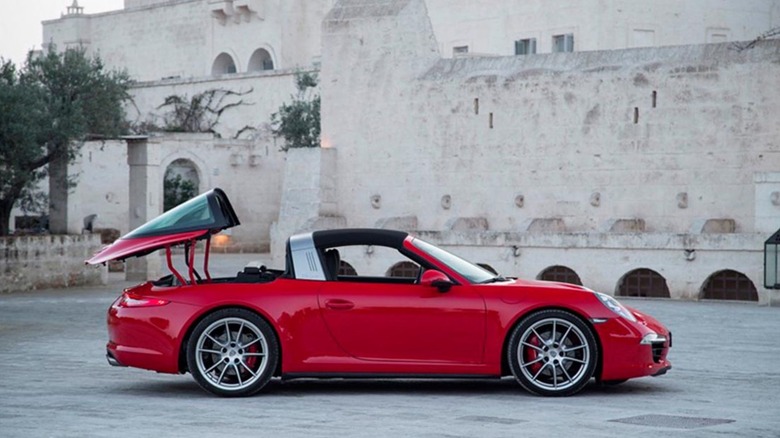 A 991 generation porsche Targa S with its roof opening system in process standing in front of an old building.