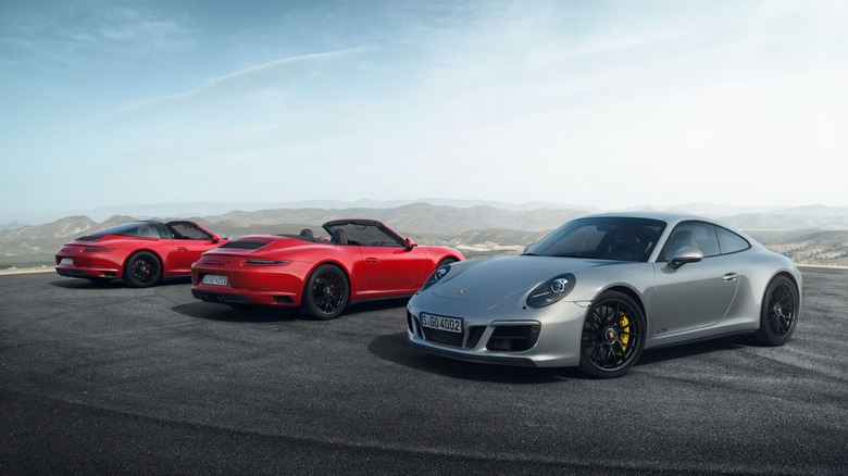 Two red and one silver Porsche 911 model from the 991.1 generation cars in different body styles parked on a road.