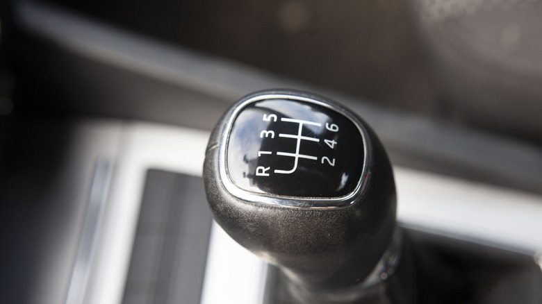 A close up shot of a black 6-speed gear shifter knob in the inside of a car.