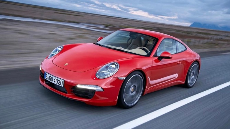 A red 991.1 generation 911 Carrera Coupe base model from 2011 moving at speed down a road.