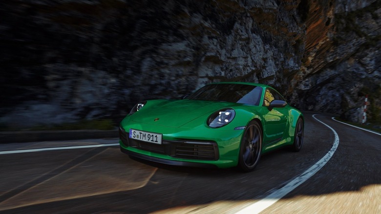 A green 992.1 Porsche 911 Touring moving through a tunneled mountain road that twists and turns in the afternoon.