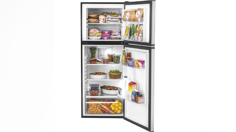 A Haier-brand top-freezer refrigerator with the doors open, showing a bunch of groceries inside
