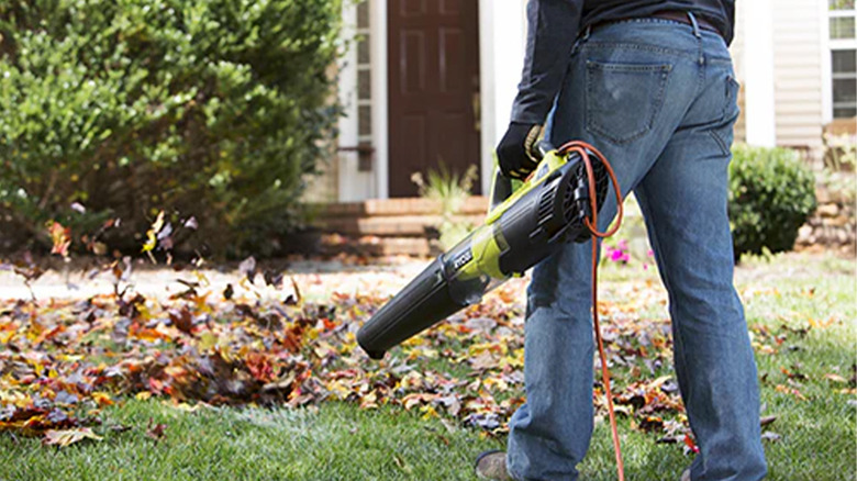 A man using a corded Ryobi leaf blower to blow leaves