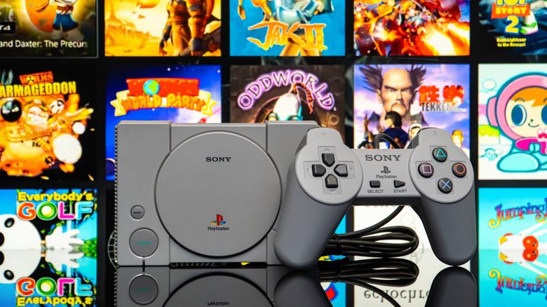 The first PlayStation console and controller, with a bunch of its games floating behind it