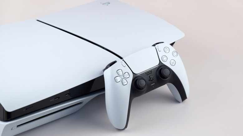 The PlayStation 5 console and a DualSense controller leaning next to it on a cream-colored surface
