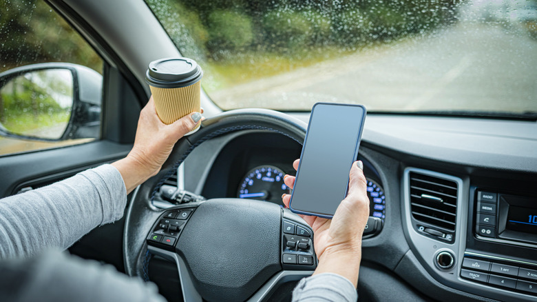 A distracted driver holding a coffee in one hand and a smartphone in the other