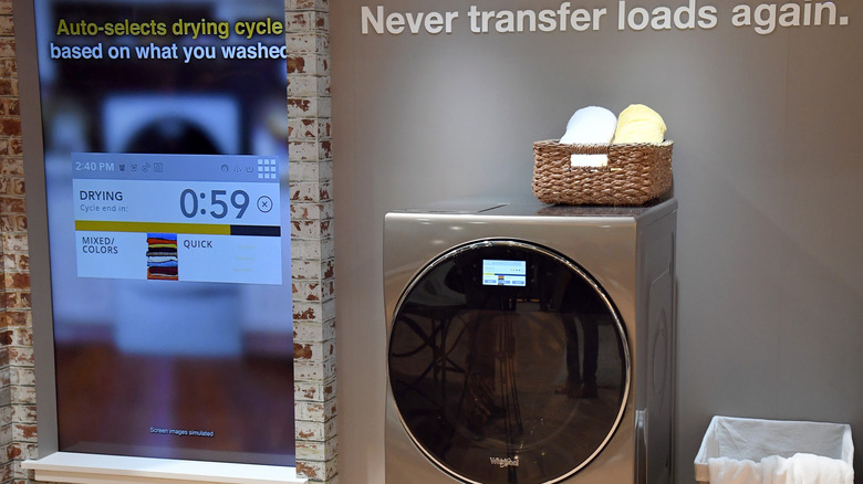 A grey combo washer and dryer unit with a dark circular glass door and a basket of folded towels on top.