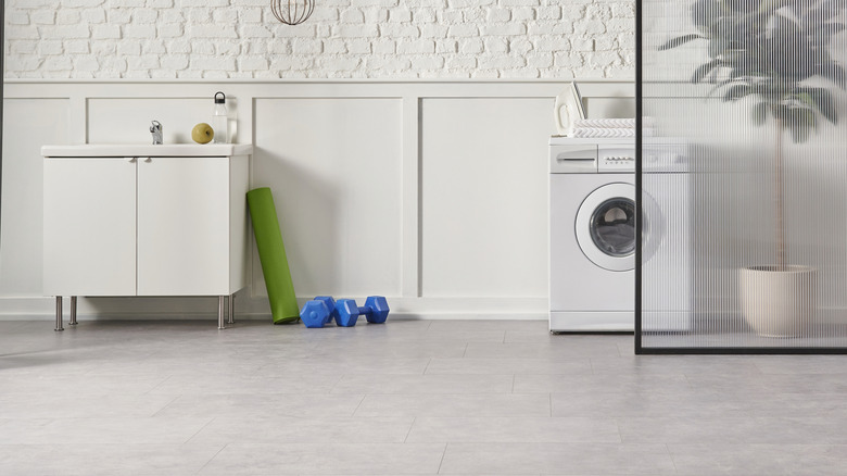 A white compact front-load washer sits against a white brick wall in a minimalist laundry space.