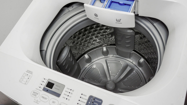 A top-down view of a top-load impeller washing machine with open detergent drawers.