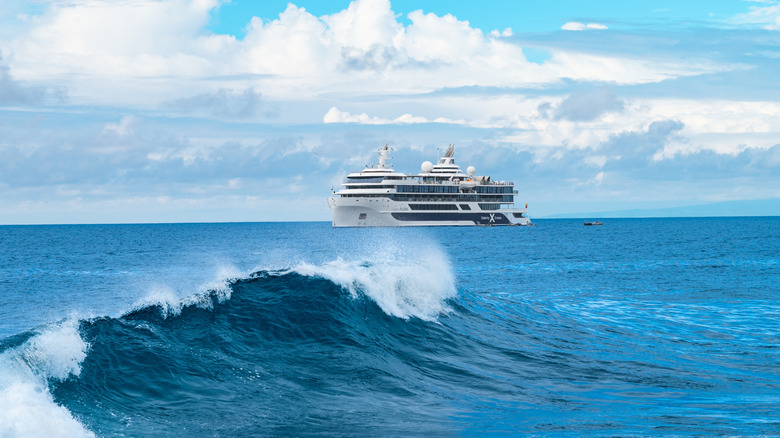 A large white cruise ship at sea with waves in the foreground