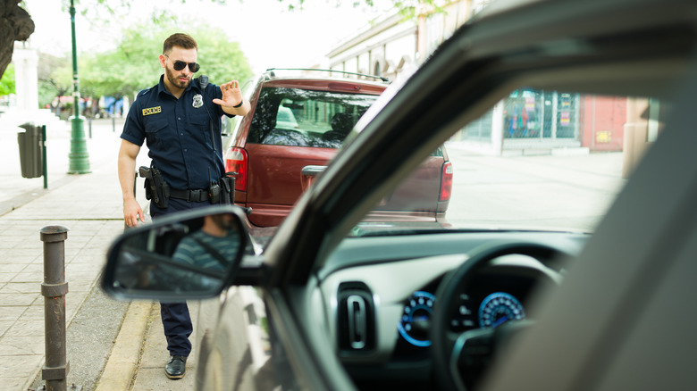 A cop making a stop gesture with his hand to a driver in his car to deliver a traffic ticket for parking.