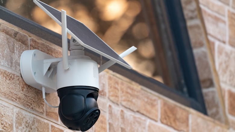 A solar-powered security camera attached to a brick wall near a window