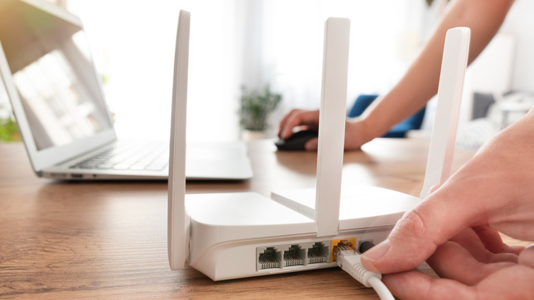 Person connecting modern wi-fi router on light table in living room