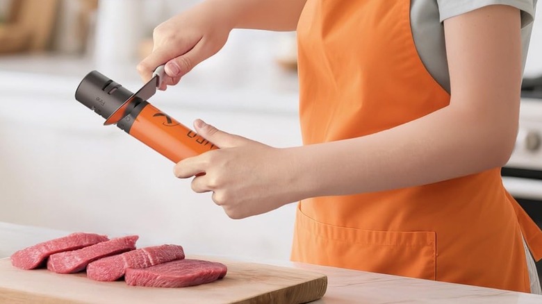 Person sharpens knife with LEFUGO sharpener above steak