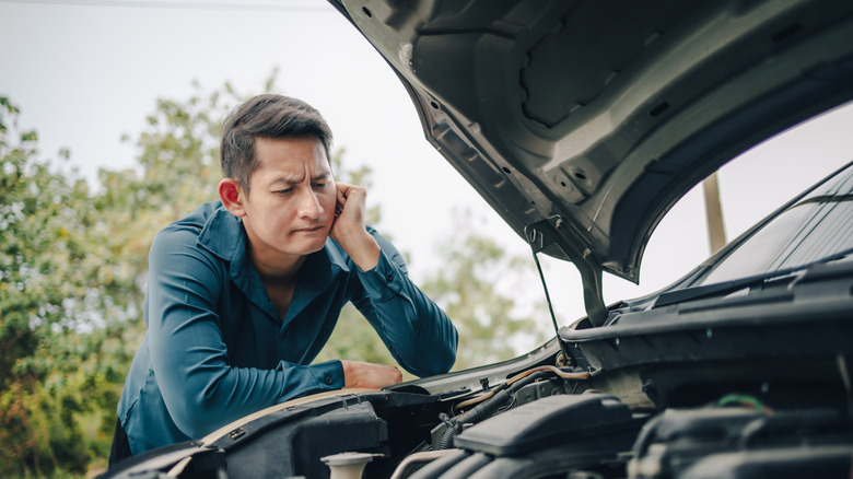 A Confused Man Standing over An Open Car Hood And Staring At An Engine