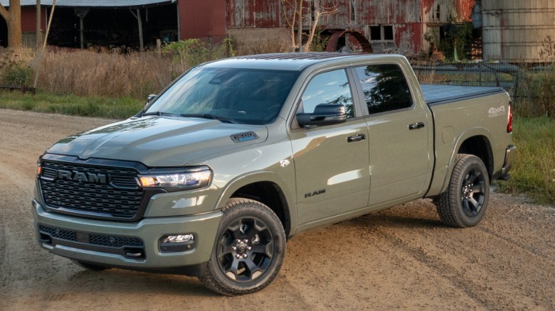 Olive green Ram 1500 parked on a dirt road in front of a farm building.
