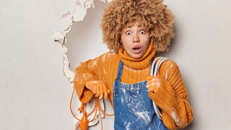 Woman holding extension cord next to broken wall