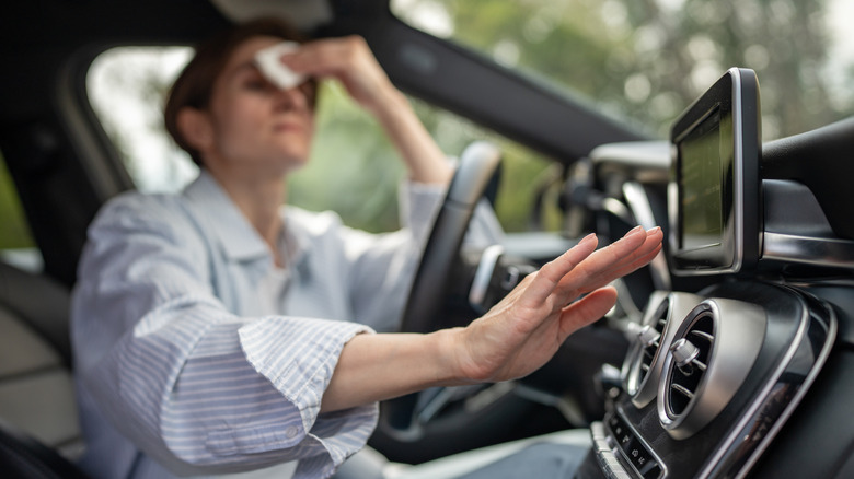 woman sweating and reaching for AC in hot car