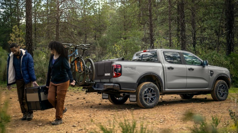 Two people unloading camping gear from a gray Ford Ranger in the forest