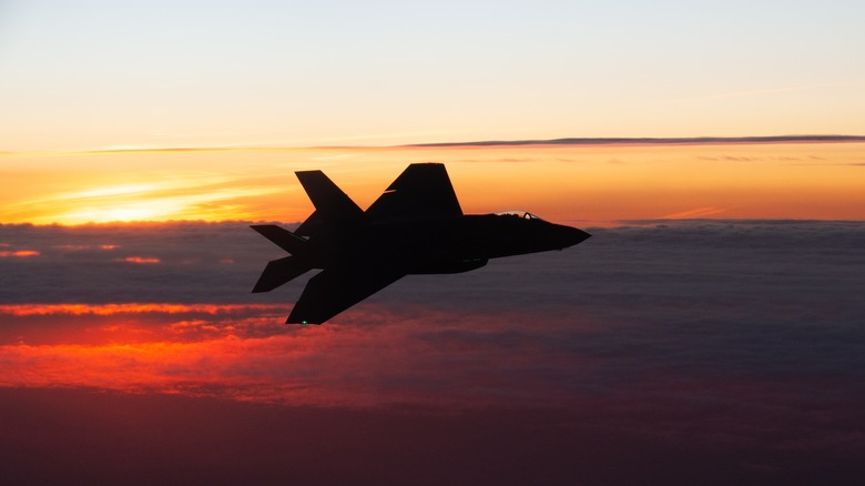 An F-35 soars above the clouds at sunset