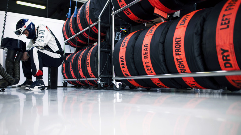 Racks of Formula One tires in blankets in garage with engineer servicing components