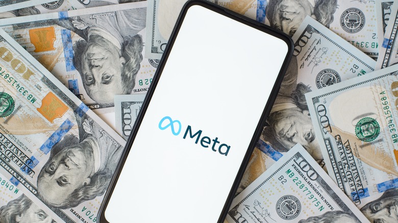 Meta logo on phone laid on top of several $100 bills