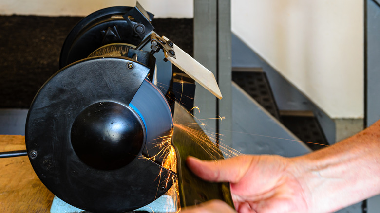 Man sharpening lawn mower blade against a spinning bench grinder