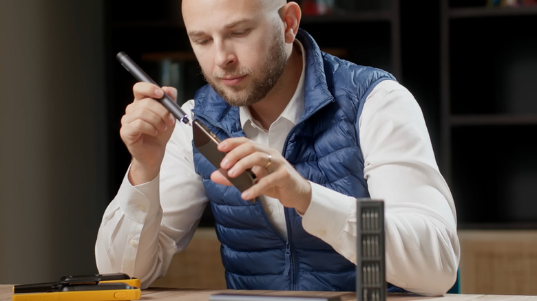 Man wearing a white button down shirt and blue quilted vest using the Fanttik E1 Max 3.7V Electric Screwdriver to tinker on a phone.
