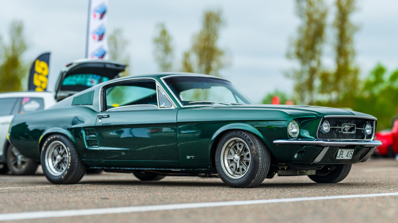 A green 1967 Ford Mustang Fastback at a open air car show, front 3/4 view