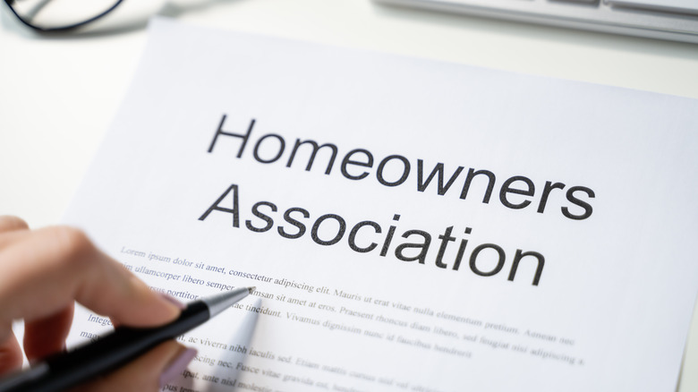 A woman's hand holding a pen over homeowner's association paperwork