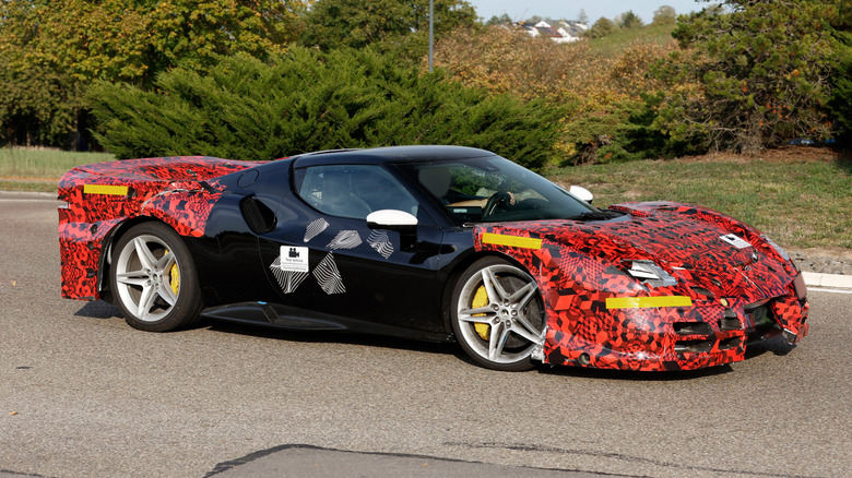 A camouflaged version of a new Ferrari 296 Challenge Stradale driving on a public road.