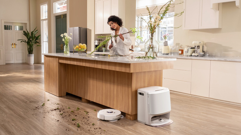 Smiling woman arranges flowers in a bright white kitchen while the Narwal Freo Z10 vacuums up the plant trimmings