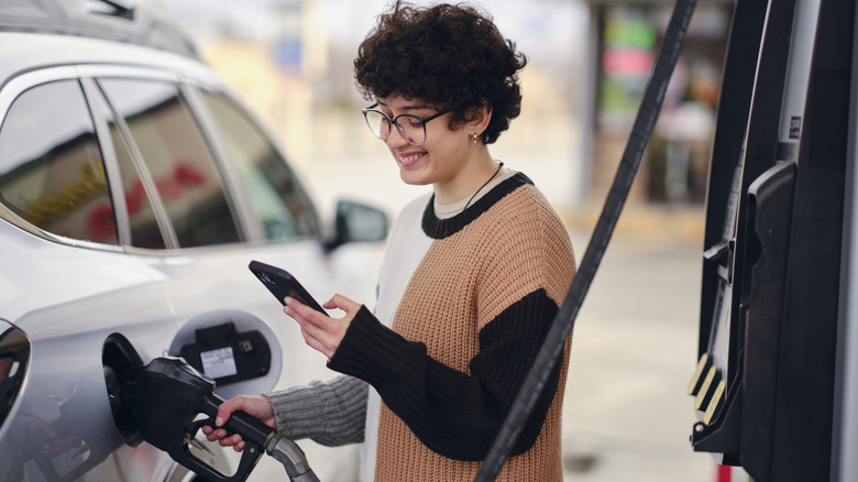 Person checking their phone while refueling car