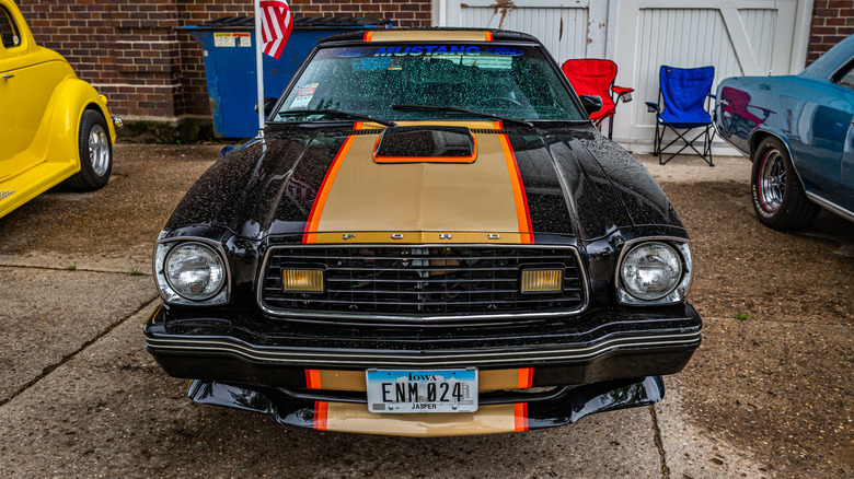 A front-facing two-tone 1970s Ford Mustang parked on a driveway.