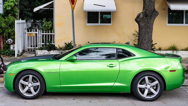 A side profile view of a bright green Chevrolet Camaro parked in front of a yellow house.