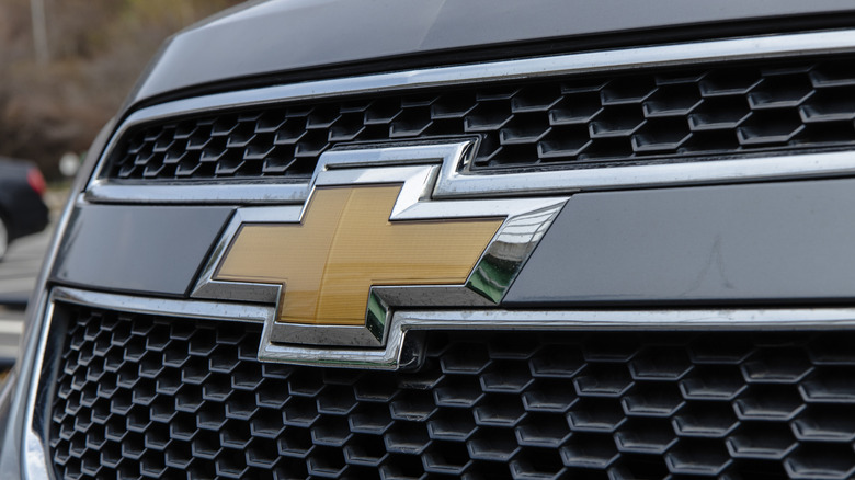A close-up of a gold Chevrolet badge placed on the front grille of a gray vehicle.