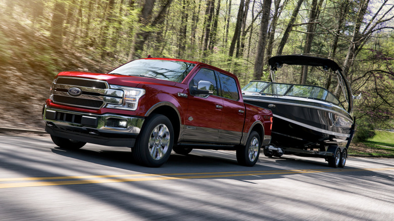 A red 3.0 Powerstroke Ford F-150 towing a boat on a country road.