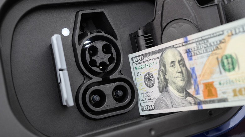 Close-up of an electric car charge port with a $100 bill.