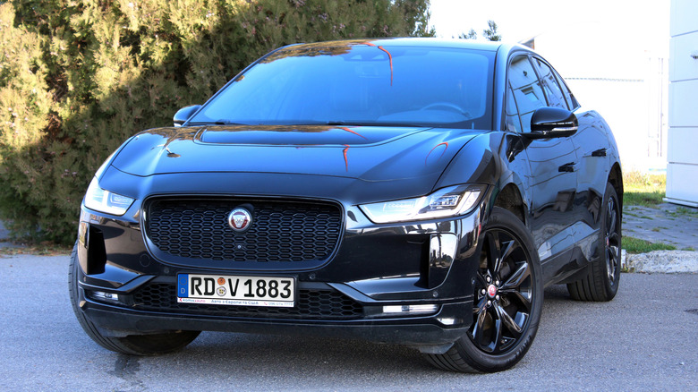 A black Jaguar I-Pace EV parked in front of bushes and a building.