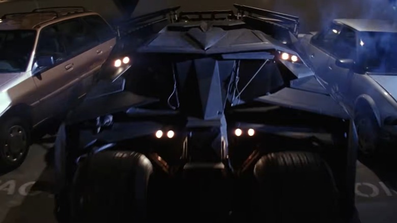 The Tumbler Batmobile wedged between two parked cars in Batman Begins.