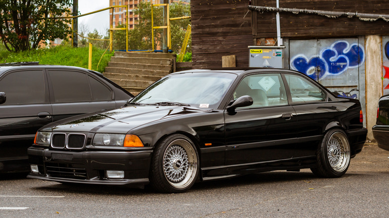 A front three-quarter view of a tuned black BMW E36 parked in an urban setting.