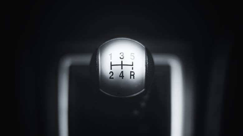 A close-up view of the upper part of a manual transmission gear lever, showing the numbered shift pattern.