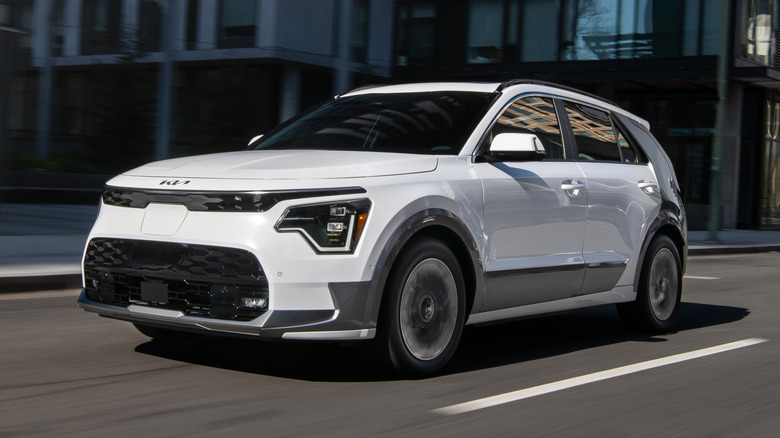 A white Kia Niro EV driving through city streets.