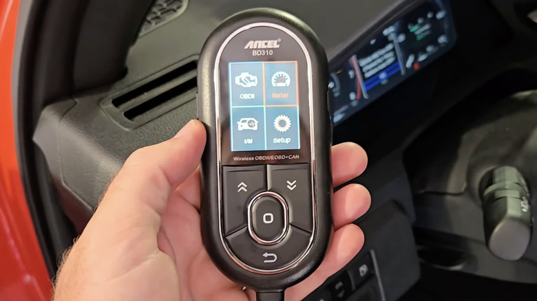 A person holding an ANCEL OBD-II scanner with a car's interior in the background.