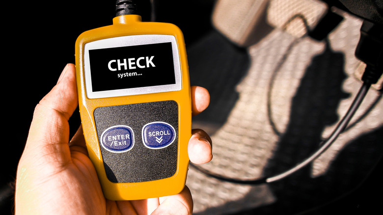 A person holding an OBD-II car diagnostics scanner checking for codes.