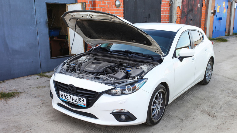 A white Mazda3 hatchback parked with its hood open.