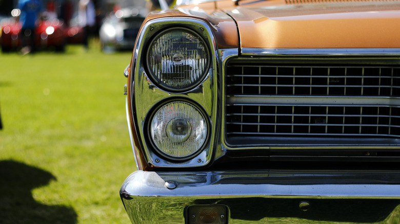 A close-up of a vintage car front left headlight and gold paint glistening in the sun.
