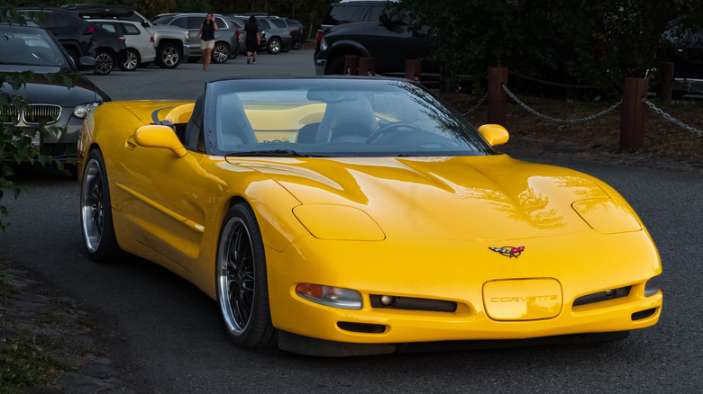 A yellow C5 Corvette with black wheels parked on a busy roadside.