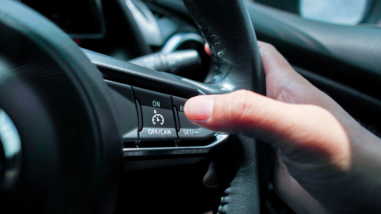 A person using steering wheel buttons to turn on cruise control.
